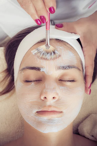 Cosmetician applying facial beauty mask for woman at spa salon