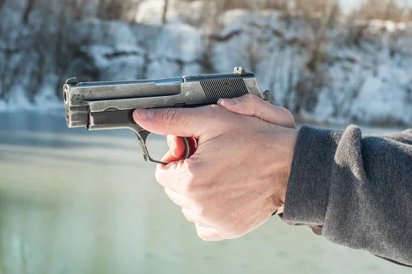 Shooter trzymając pistolet i strzelanie na tle wody jeziora zimą — Zdjęcie stockowe