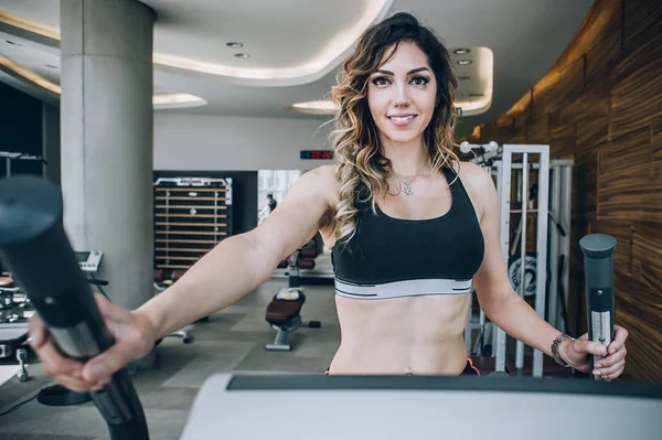 Attractive muscular smiling fitness woman running on treadmill i