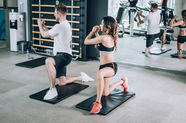 Attractive fitness woman with coach doing hard exercise in gym