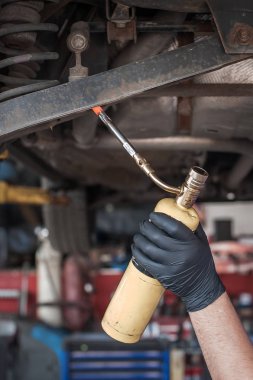 Araba ustası tamirci vidaları alev topuyla ısıtıyor.