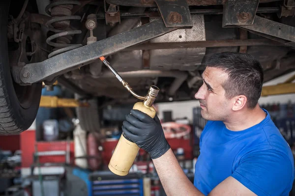 Reparador mecánico maestro de coches calentando los tornillos con flamethrowe —  Fotos de Stock