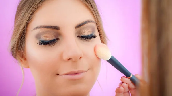 Make-up kunstenaar het aanbrengen van make-up op haar gezicht met behulp van poeder borstel — Stockfoto