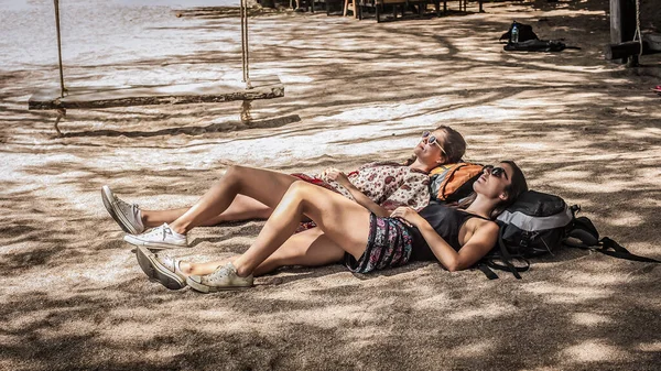 2人の女の子の友人バックパッカー楽しんで横たわっ彼らの牧場熱帯ビーチ砂の上に日陰で — ストック写真