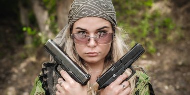 Güzel ve çekici kadın asker iki silahla poz veriyor. Silahlı bir kadın. Atış poligonu talimi. Moda modeli tarzı