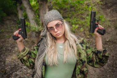 Güzel ve çekici kadın asker iki silahla poz veriyor. Silahlı bir kadın. Atış poligonu talimi. Moda modeli tarzı