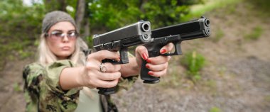Çekici kadın asker, iki silah zoruyla atış talimi yapıyor ve saldırgana nişan alıyor. Soyut yakın plan tabanca geniş açı ön görüntüyü gösteriyor. Doğa.