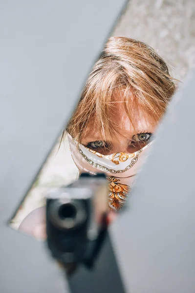 Female gangster bandit with headscarf over her face holding gun and gun point aim through barricade. Close-up front view