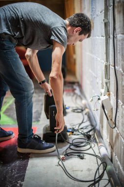 Tiyatro ışıklandırma teknisyeni elektrik mühendisi sahne arkasındaki aydınlatma elementlerinin odak noktasını ayarlıyor. Tiyatrodaki spot ışıkları. Sahnenin arkasında.