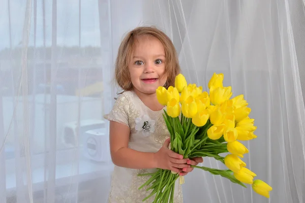 屋内に黄色いチューリップを持つ小さな女の子 — ストック写真