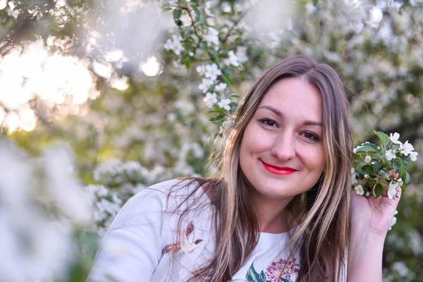 Mujer de pelo largo y rubio en el jardín con flores. Hermosa chica en un día soleado . — Foto de Stock