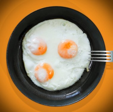Turuncu bir arka plan üzerinde dökme demir tavada üç yumurta kahvaltı. Yukarıdan görüntüle.