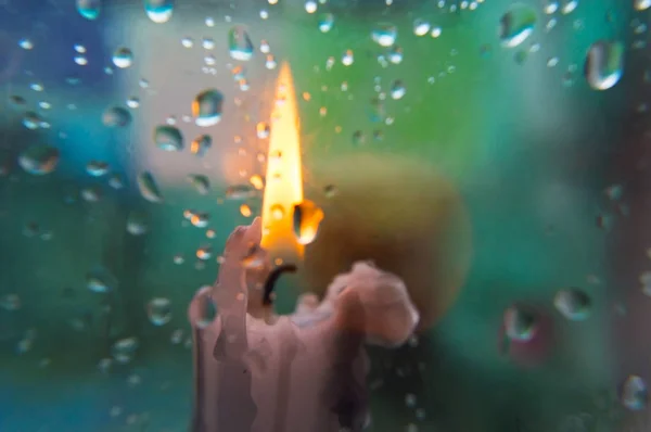 Gocce di pioggia su vetro e sfondo sfocato con una candela nella parte anteriore — Foto Stock