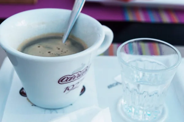 Uma xícara de café e uma colher com um copo de água fria . — Fotografia de Stock