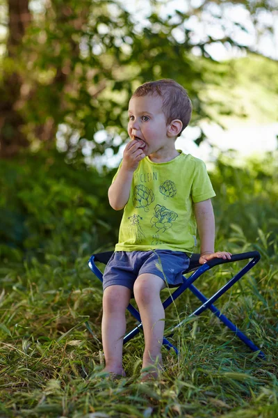 Забавный ребенок, очаровательный блондинка мальчик в желтой футболке сидя на открытом воздухе в саду в солнечный летний день — стоковое фото