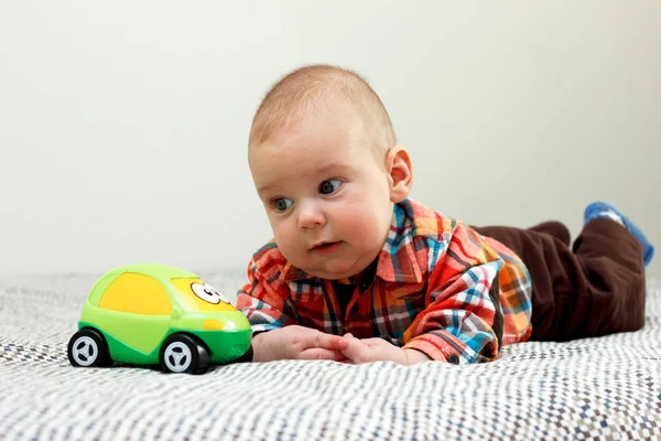 The baby boy is playing with a green little car plaid shirt — Stock Photo, Image