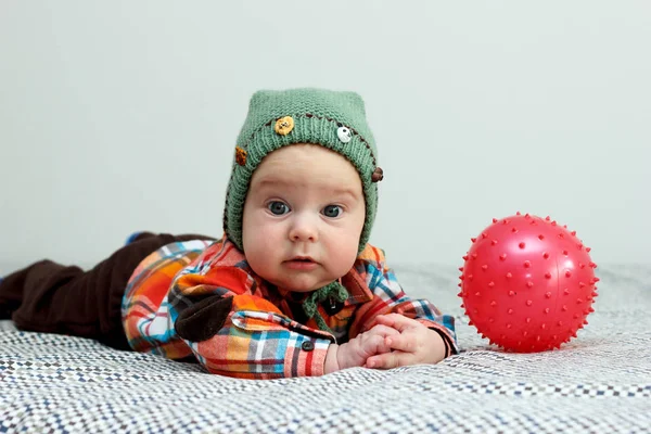 El niño está jugando con una pequeña camisa a cuadros roja bola, sombrero verde —  Fotos de Stock