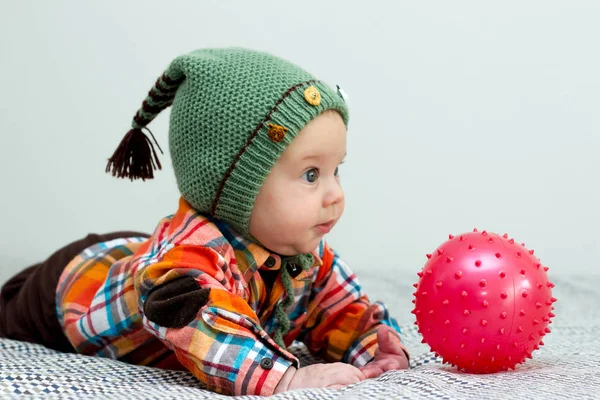 El niño está jugando con una pequeña camisa a cuadros roja bola, sombrero verde —  Fotos de Stock