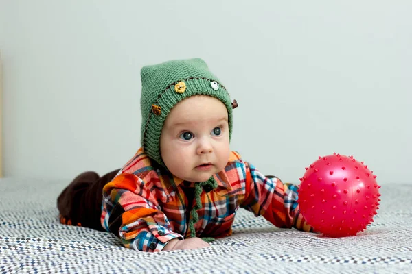 El niño está jugando con una pequeña camisa a cuadros roja bola, sombrero verde —  Fotos de Stock