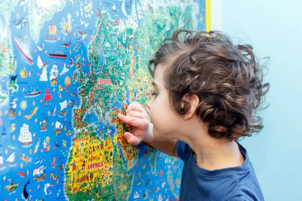 Кудрявый ребенок с интересом смотрит на голубую карту мира — стоковое фото
