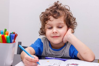 Küçük kıvırcık çocuk oturur bir masada, gülümsüyor, vardır bir dinlenme harften sonra gözler kapalı. Gerçekleştirilen çalışma - dinlenmek mümkün mü.