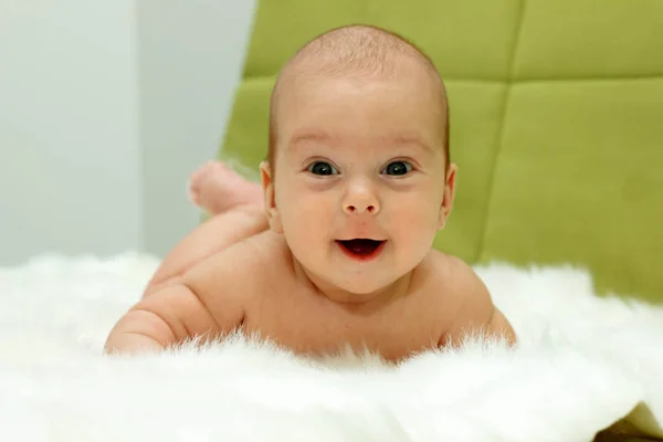Bebé acostado en una piel blanca, mira a la cámara y sonríe —  Fotos de Stock