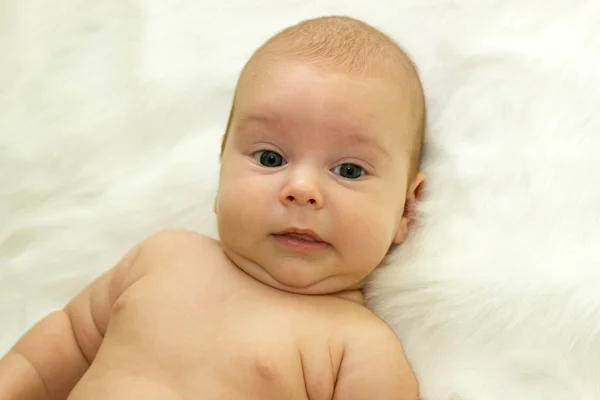 Baby lying on a back on a white fur, look into the camera and smile — Stock Photo, Image