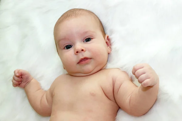 Baby lying on a back on a white fur, look into the camera and smile. HIs handles are lifted — Stock Photo, Image