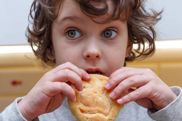 Un enfant frisé de cinq ans mange des biscuits avec appétit dans la cuisine — Photo