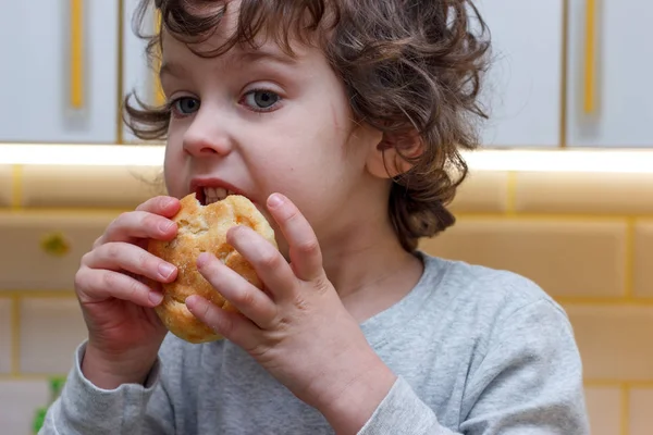 Un enfant frisé de cinq ans mange des biscuits avec appétit dans la cuisine — Photo