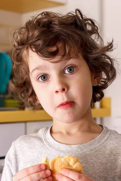 Un enfant frisé de cinq ans mange des biscuits avec appétit dans la cuisine — Photo