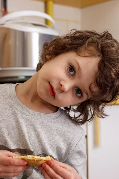 Un enfant frisé de cinq ans mange des biscuits avec appétit dans la cuisine — Photo