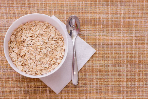 Copa con harina de avena cruda en servilleta blanca sobre fondo de pistola para un desayuno saludable —  Fotos de Stock