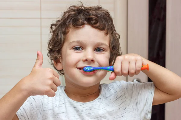 Sevimli küçük çocuk diş fırçası ile dişlerini fırçalama ve başparmak gösteren. Çocuk sağlığı kavramı, tıp.
