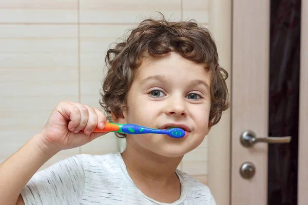 Menino feliz escovando os dentes no banheiro na frente do espelho, higiene oral — Fotografia de Stock
