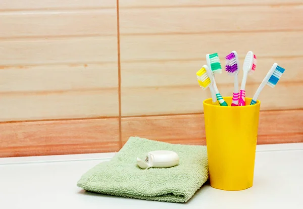 Toothbrushes in yellow glass, dental floss and towel, space for rext — Stock Photo, Image