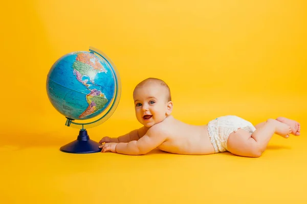 Little baby playing with globe on yellow background — Stock Photo, Image