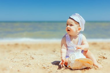 Kumsalda elinde deniz kabuğu olan bebek.