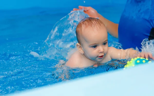 Coach teaches the baby to swim in the pool. baby splash in the water in the pool. The concept of a healthy