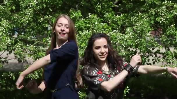 两个女孩在绿色树叶的背景下进行舞蹈比赛 年轻女子在镜头前鬼混 — 图库视频影像