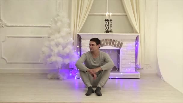クリスマス ツリー ガーランドの背景にヨガのポーズで床に座っている人 — ストック動画