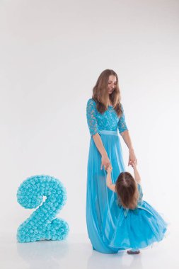 Anne ve çocuk beyaz bir arka plan üzerinde poz. Kadın ve mavi elbiseli kız oyun