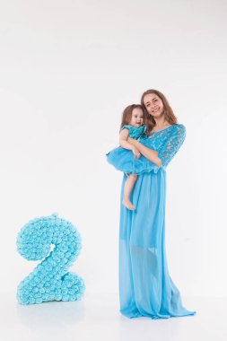Anne ve çocuk beyaz bir arka plan üzerinde poz. Kadın ve mavi elbiseli kız oyun