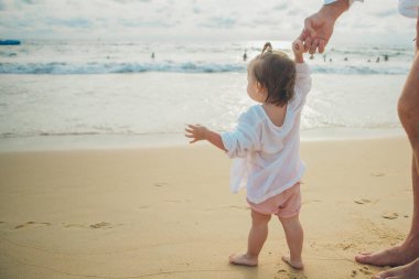 küçük bir çocuk yürümeyi, deniz kıyısında ebeveynlerin elini tuttuğunu öğrenir