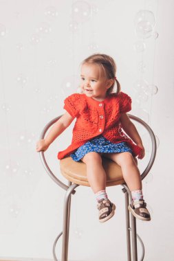 beyaz bir arka plan sandalyede oturan kırmızı ve Mavi giysili küçük kızı