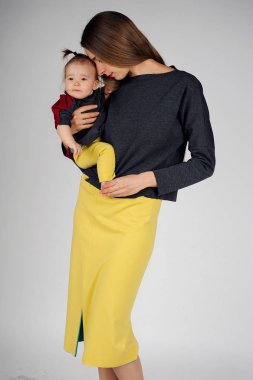 aile fotoğrafı: bir çocuk onun kollarında tutan bir kadın. Tüm aile için moda: anne ve kızı giyinmiş sarı-gri renkte. Elbise modeli gösterir