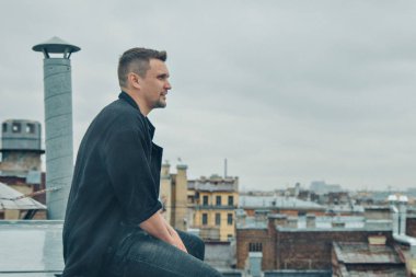 Çatının kenarında oturan yakışıklı adam