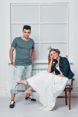 Beyaz elbiseli bir sandalyede oturan bir kız bir taç yanındaki adam makyaj ile sahanın