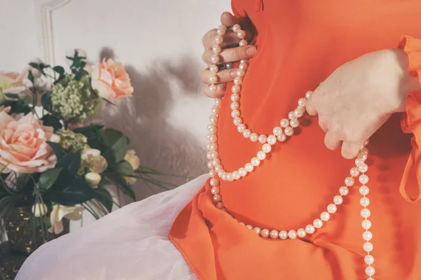 胃の背景に真珠のネックレスを保持しているオレンジのドレスに妊娠中の女性 — ストック写真