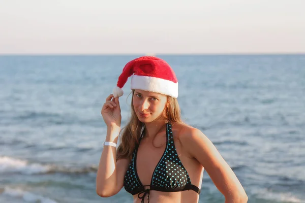 少女の水着姿は 白いポンポンを持って海の背景に赤いクリスマス帽子 — ストック写真